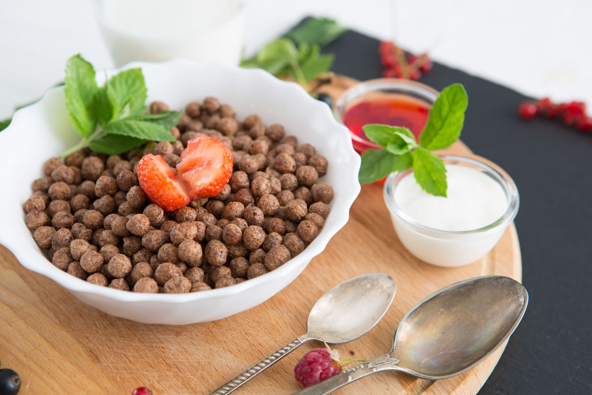 Chocolate balls in bowl with milk on rustic wooden table