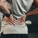 Fitness, back pain and hands of man at gym for training with muscle, problem or arthritis.